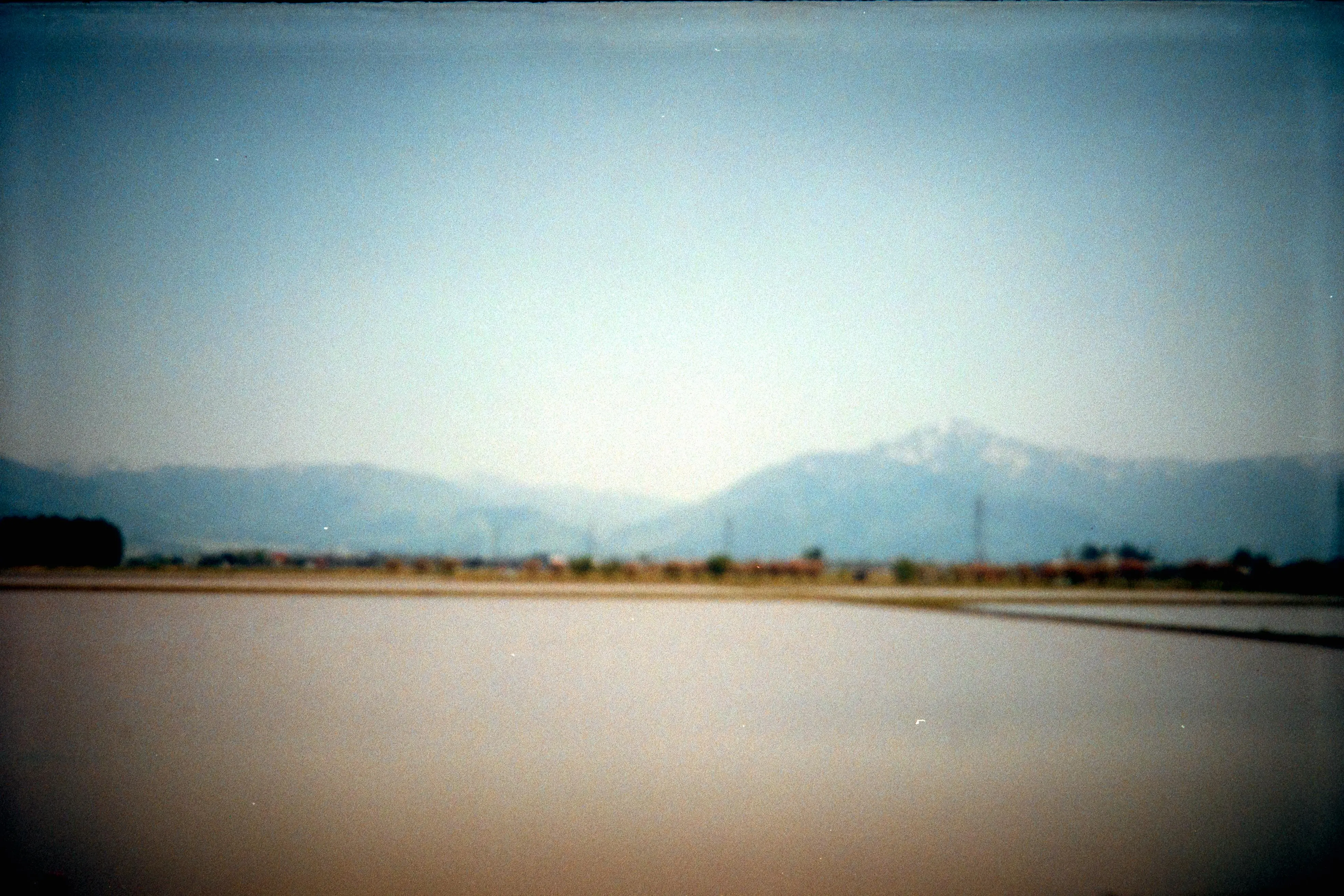 遠くの山々に向かって続く田舎道を撮影した雰囲気のあるフィルム写真。曇り空の下、柔らかい焦点と落ち着いた色調で表現されている